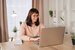 smiling woman in glasses working on laptop in home office, sitting at desk.